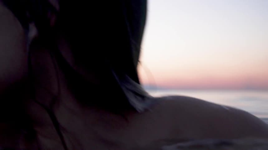 A worried looking woman skinny dips in a lake at sunset
