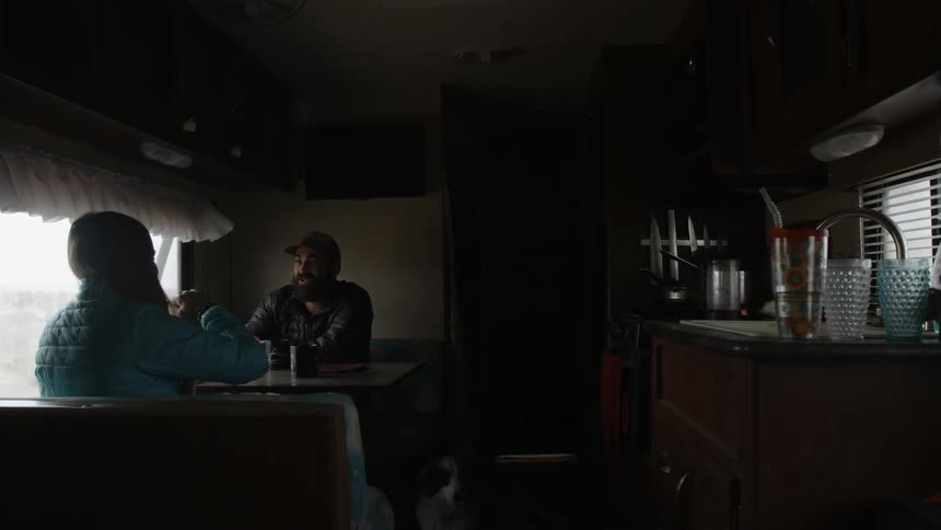 Man and woman sitting, talking and drinking at table in motorhome