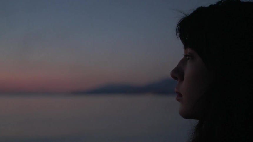 A woman looks out at a lake at sunset
