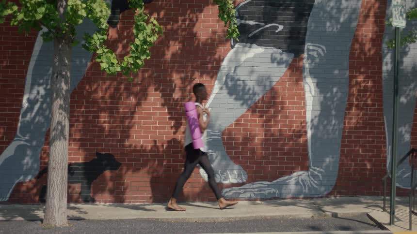 Woman walks on a sidewalk next to a brick building with a painting on it