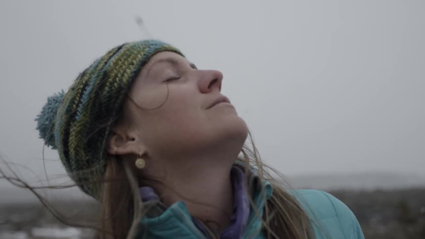 A woman stands in the wind with her eyes closed