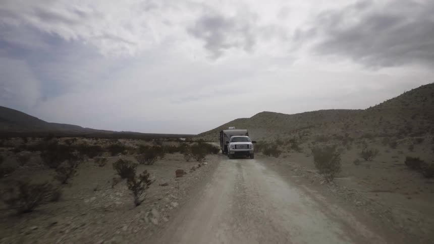 A truck hauls a camper on a dirt road in the wilderness