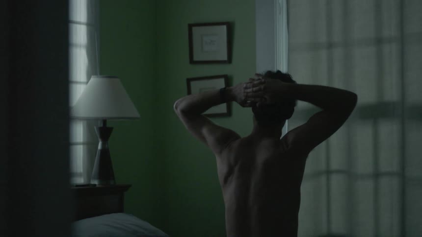 A shirtless man stretches in bed
