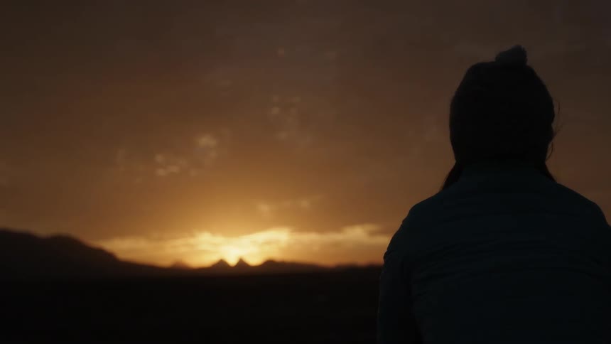 A woman looks at a sunset over mountains