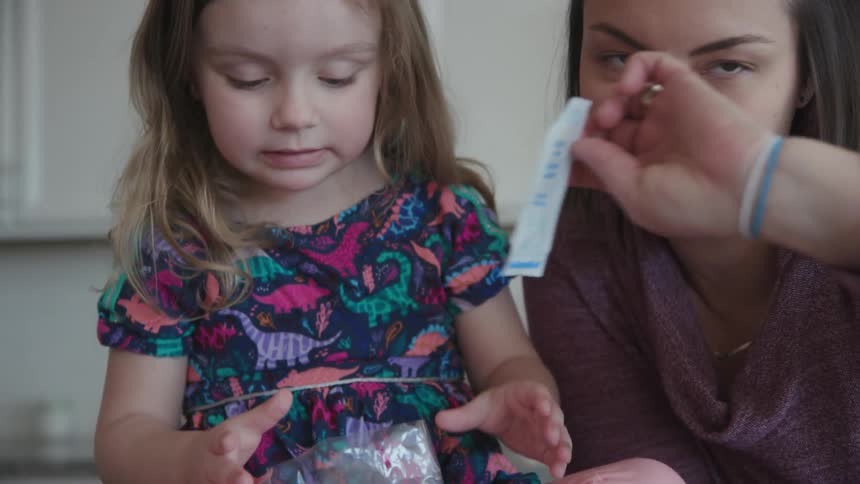 A woman helps a young girl pour dye into a bag
