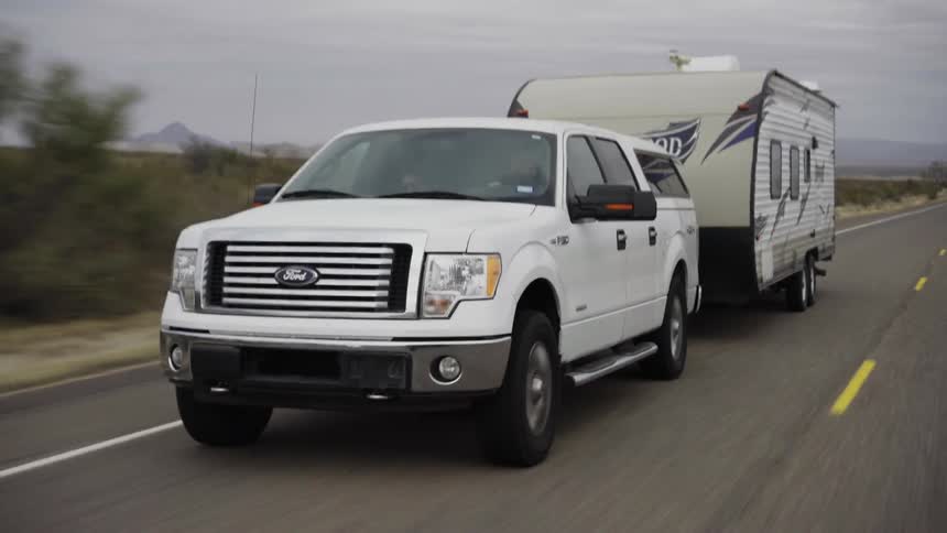 A white truck with a trailer attached drives down the street