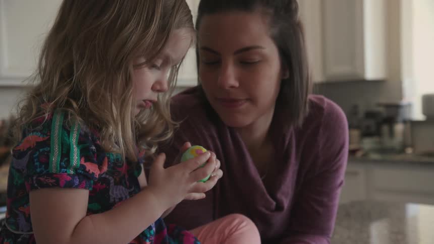 A mom and young girl decorate easter eggs in a kitchen