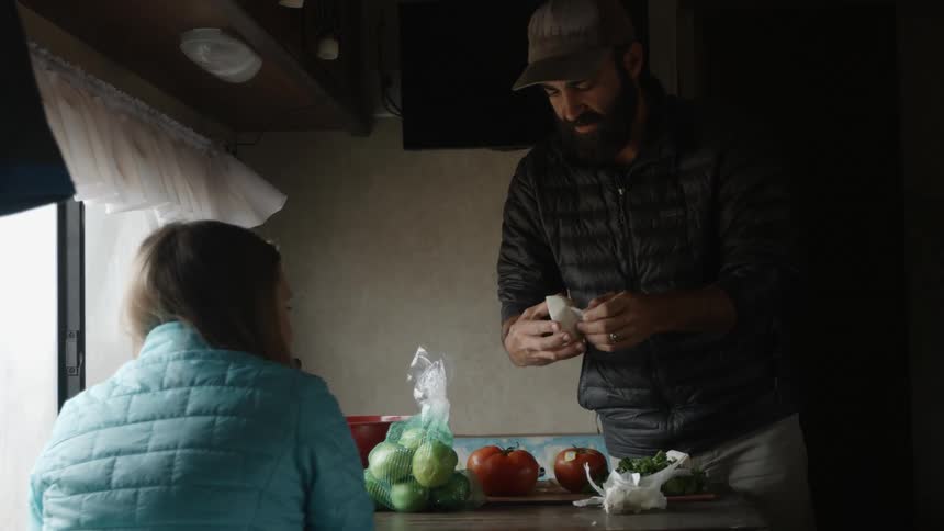 Man and woman sit at a small table talking while man peels an onion