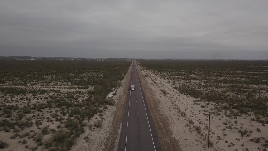 A pickup towing a camper trailer drives through a desert landscape