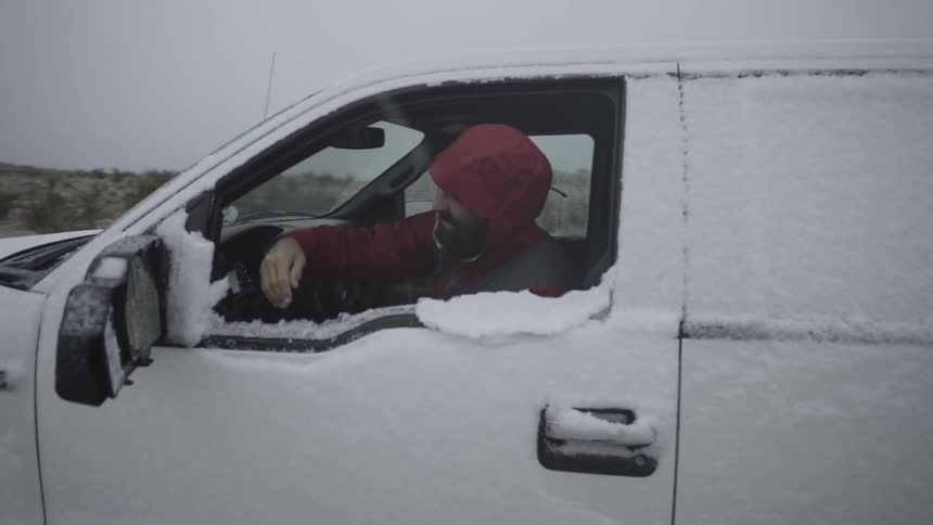 A man wipes snow off of the side of a truck