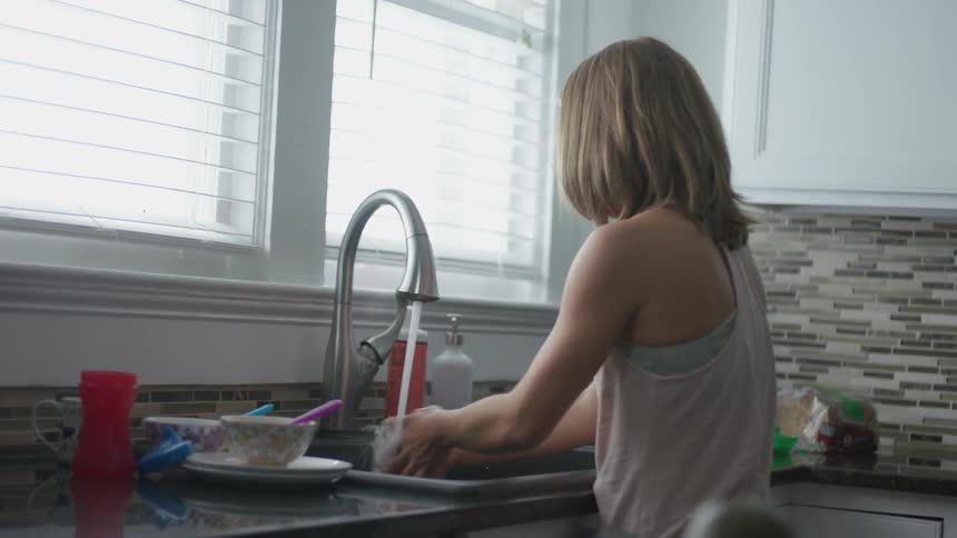 A woman washes her hands in a kitchen sink