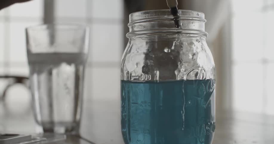 Person swirls a paintbrush around in blue water