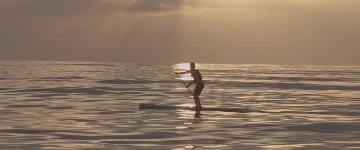 A man paddle boards on the ocean at sunset