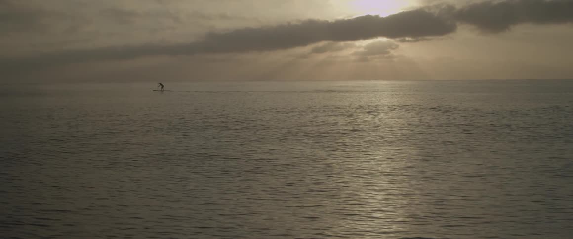 Person paddling on raft out in ocean as sun sets behind clouds