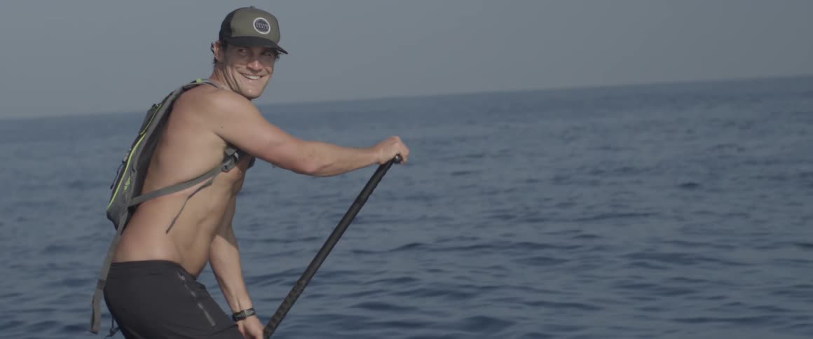 A man smiles as he paddles a stand up board out in the ocean