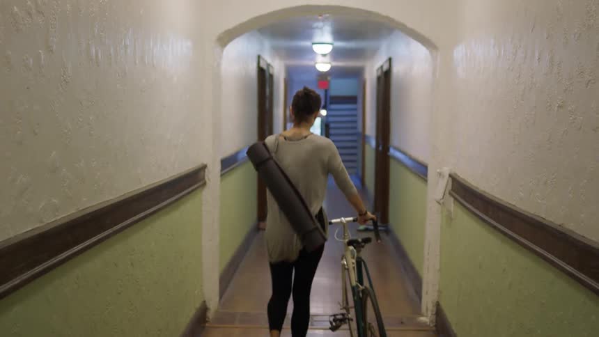 A woman carries a yoga mat and pushes her bicycle