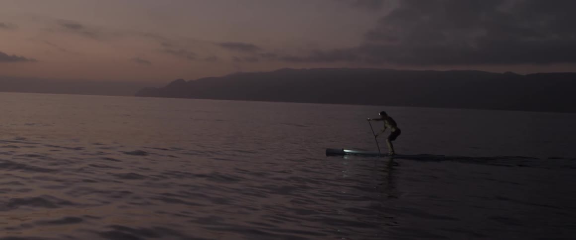 A man paddle boards on a lake at sunset