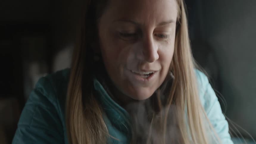 A woman takes a drink from a mug of steaming liquid