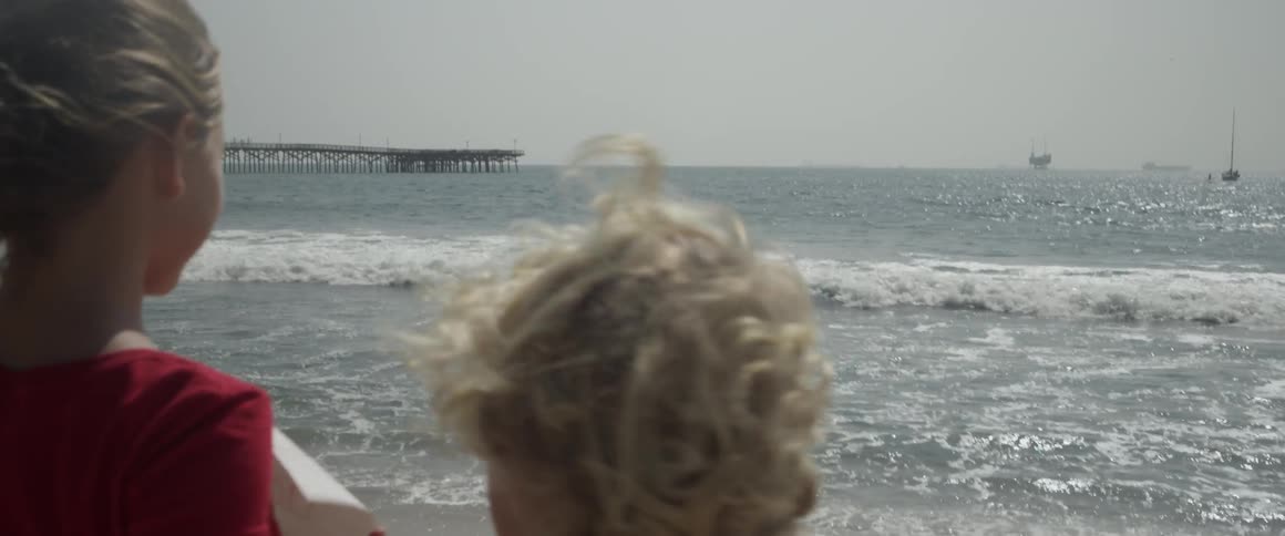 Two children stand on a beach and one waves her arms