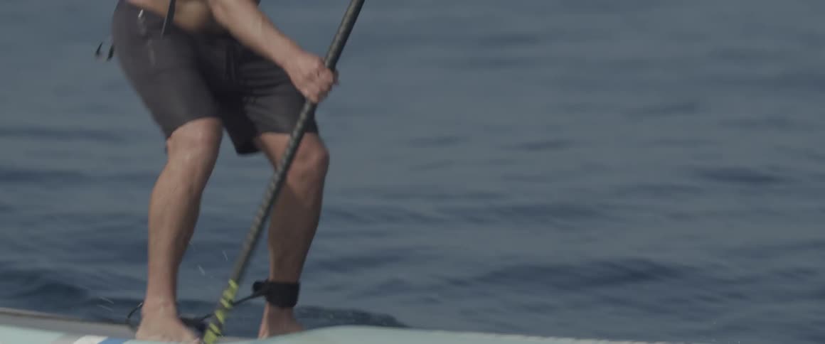 A man wearing a harness paddle boards through a body of water