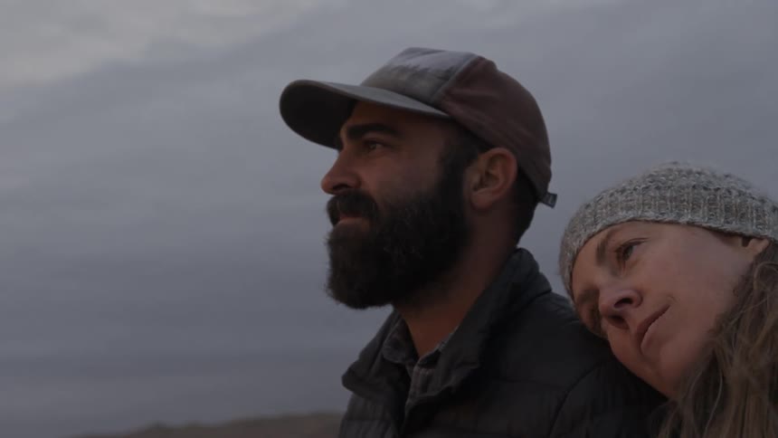A woman leans her head on a man's shoulder outside on a cloudy day