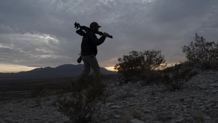 A photographer carries a tripod in the wilderness at sunset
