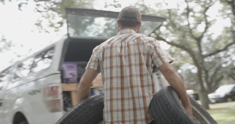 A man carries two tires to the back of a pickup truck