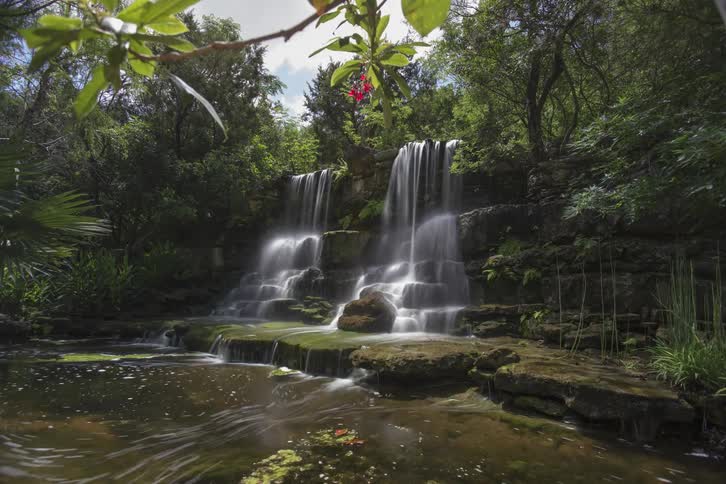 The waterfall is wide and short moving into a pond below