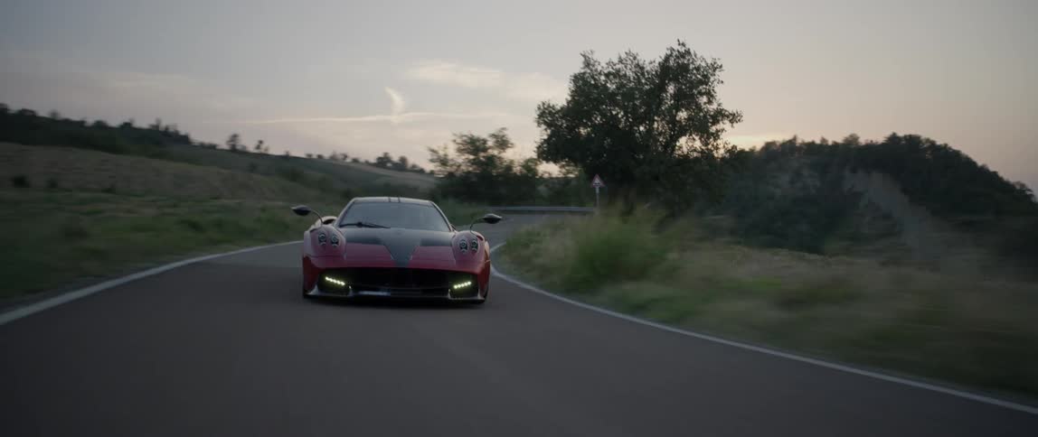 A sports car drives on a rural road at sunset
