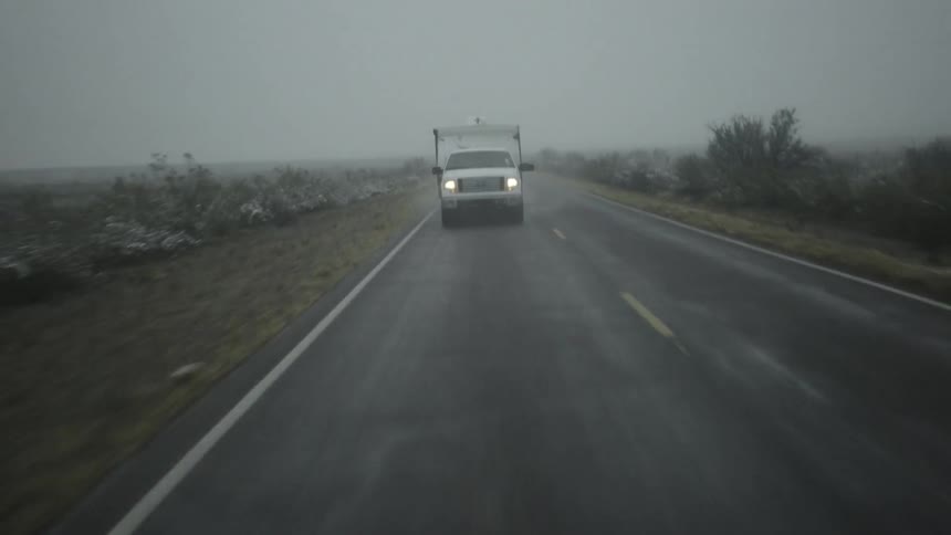 A truck pulling a trailer travels down a wet road