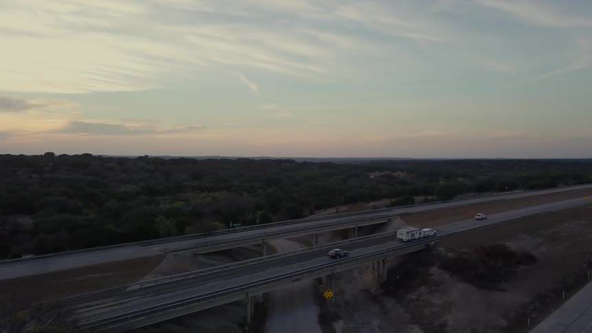 The sun is setting as people drive over the bridge