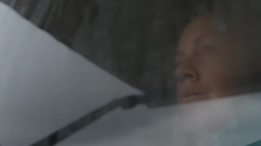A woman is staring out of a vehicle window on a wet day