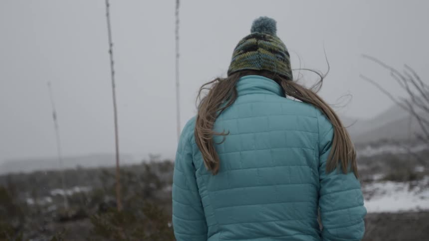 Snow falls on a woman in winter clothes walking outside