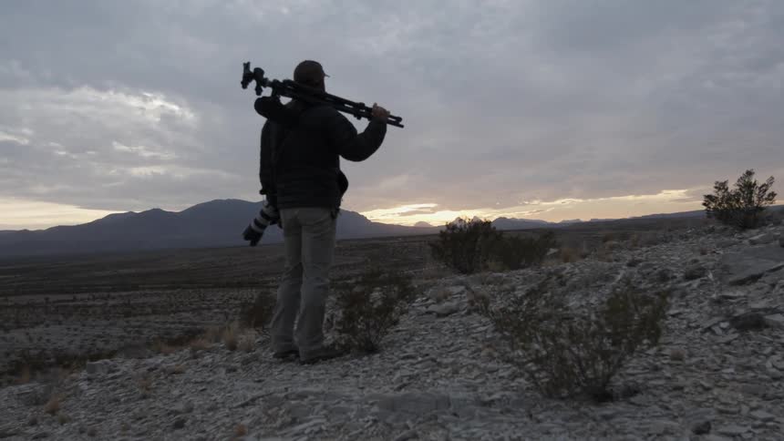 A photographer stands in a rural field while watching a sunset