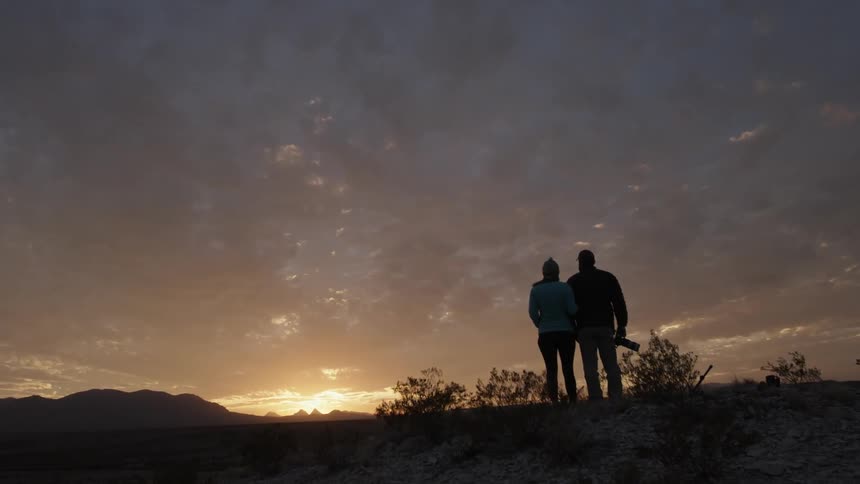 A couple watches the sunrise on a hill