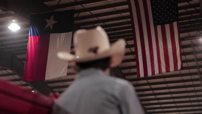 A cowboy stands beneath texas and american flags
