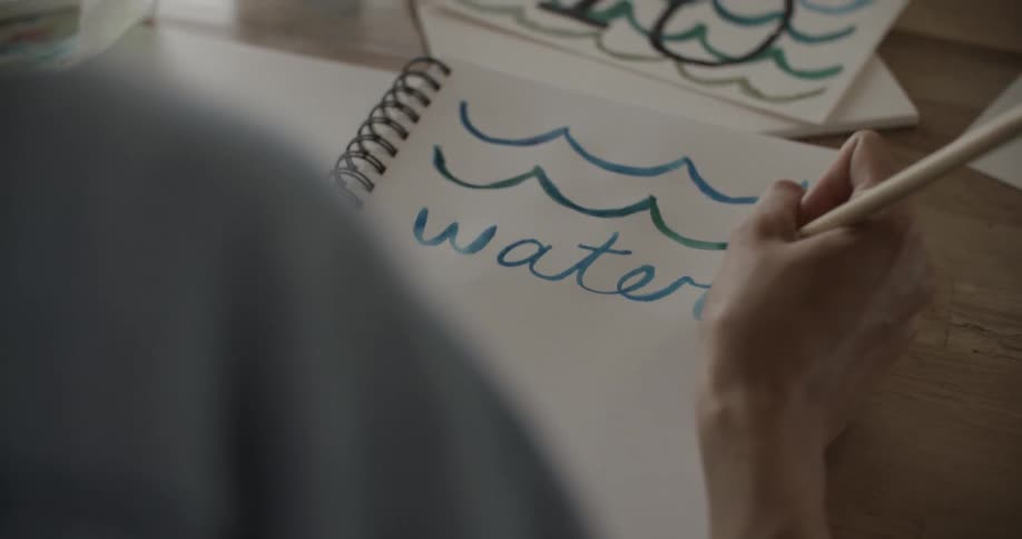 A woman writes in a notebook with a paintbrush