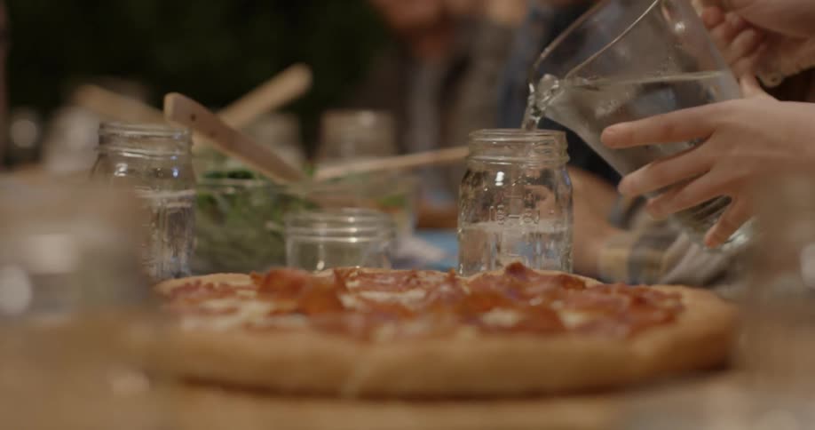 Person lifts up a water pitcher behind a pizza and pours it in a glass