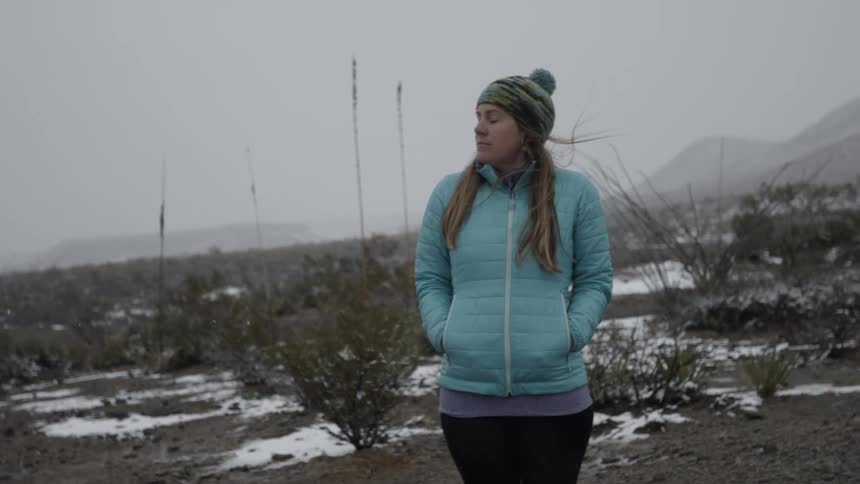 A woman stands in a rural field while it snows