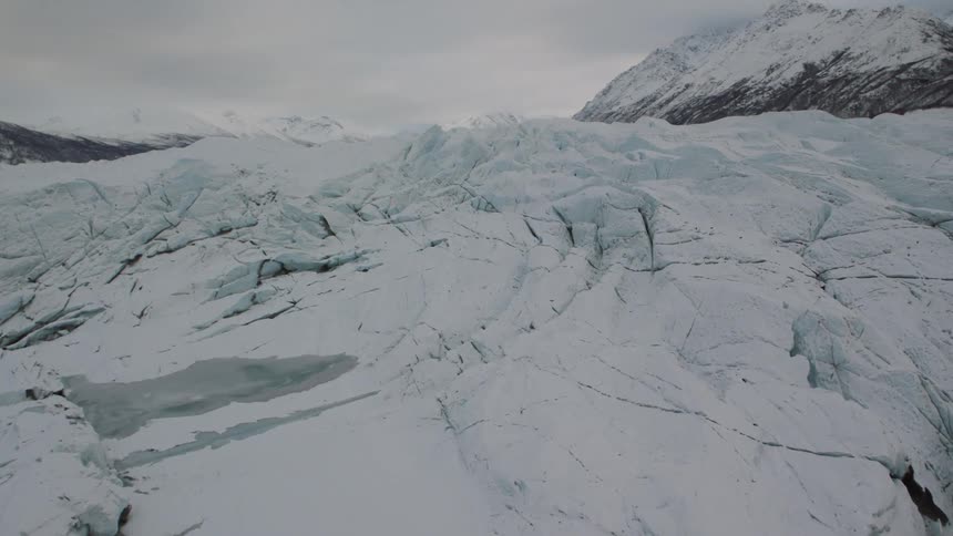 Flying over jagged glacial ice flowing between sculpted mountains