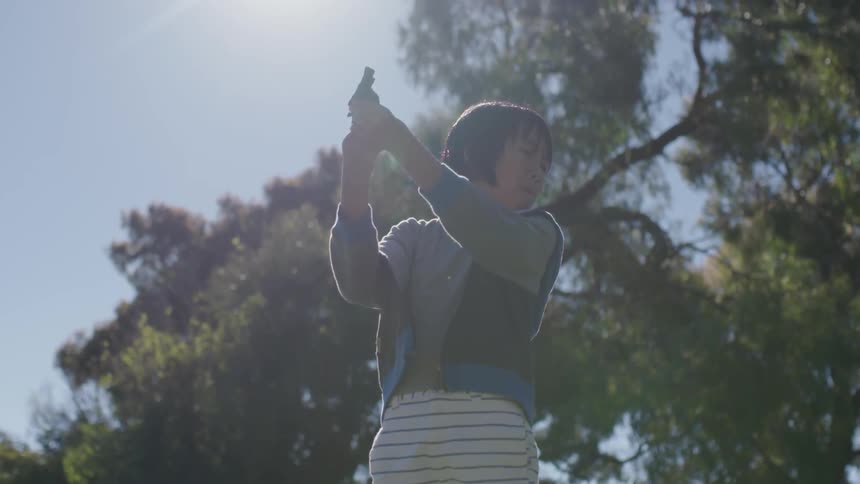 A young boy holds a gun outside on a sunny day