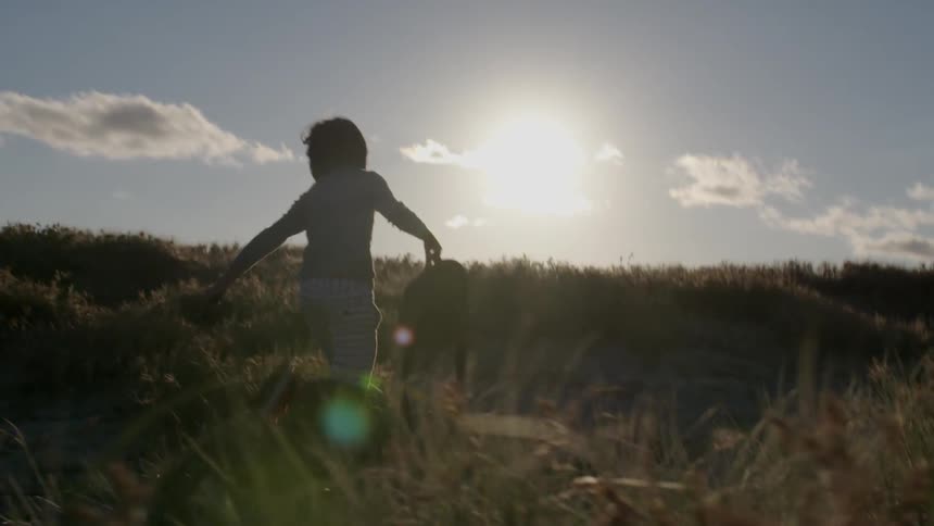 A young boy runs in a field carrying a bag
