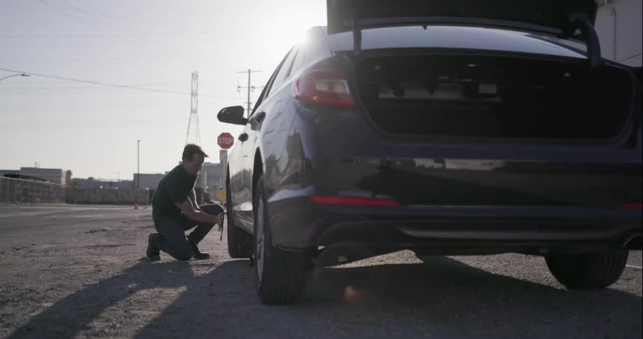 Man changes tire of his car on a sunny day