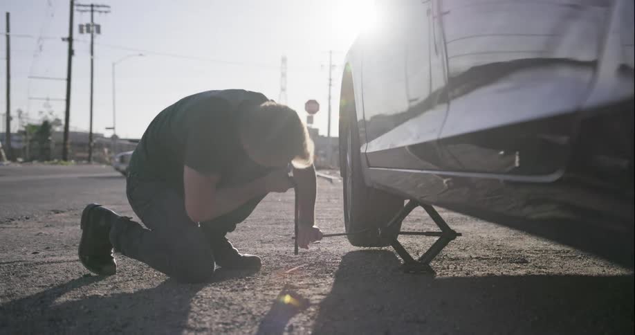 A man changes a tire on the side of the road