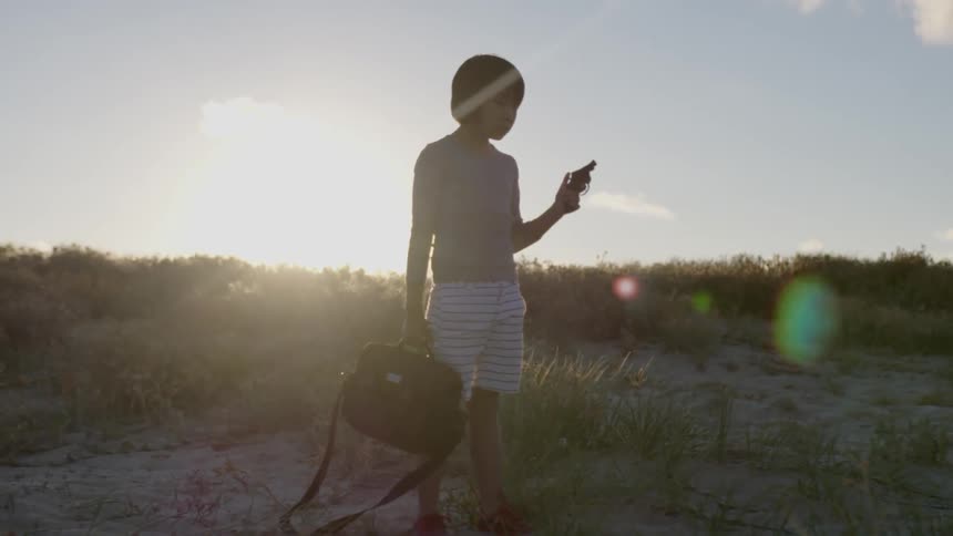 A young boy holds a gun outside at sunset