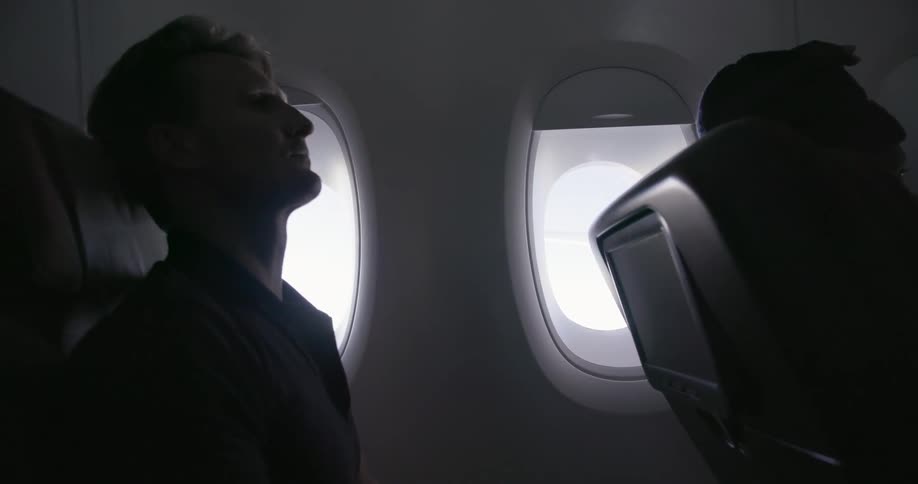 Man sitting in airplane looking out window then resting head back on seat