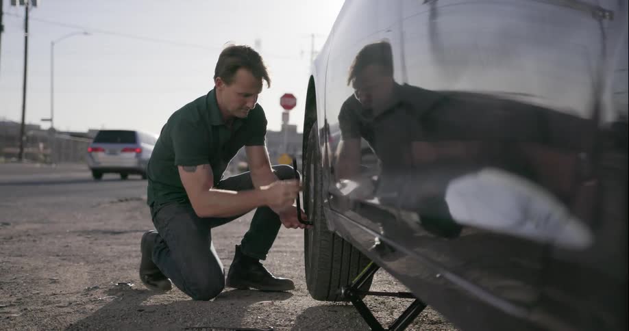 A man changes a tire on the side of the road