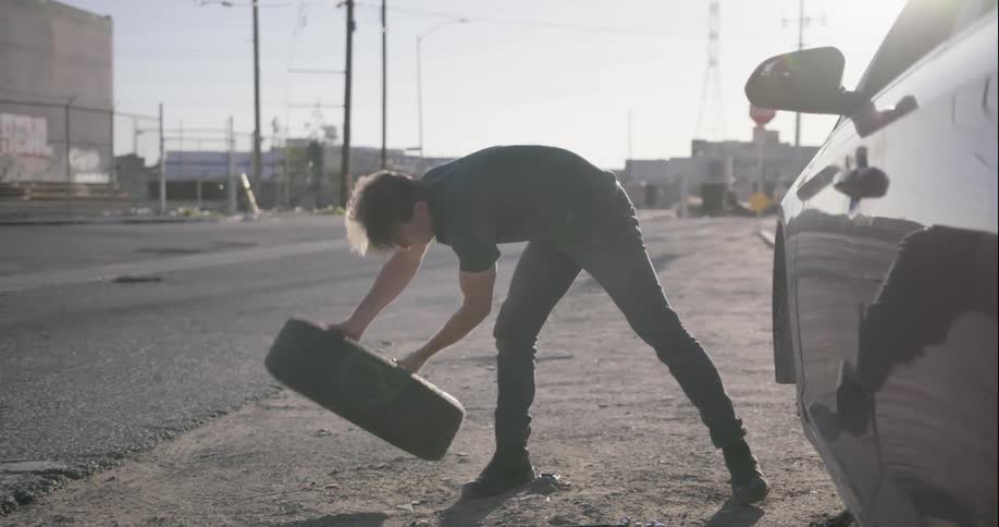 A man changes a tire on the side of the road