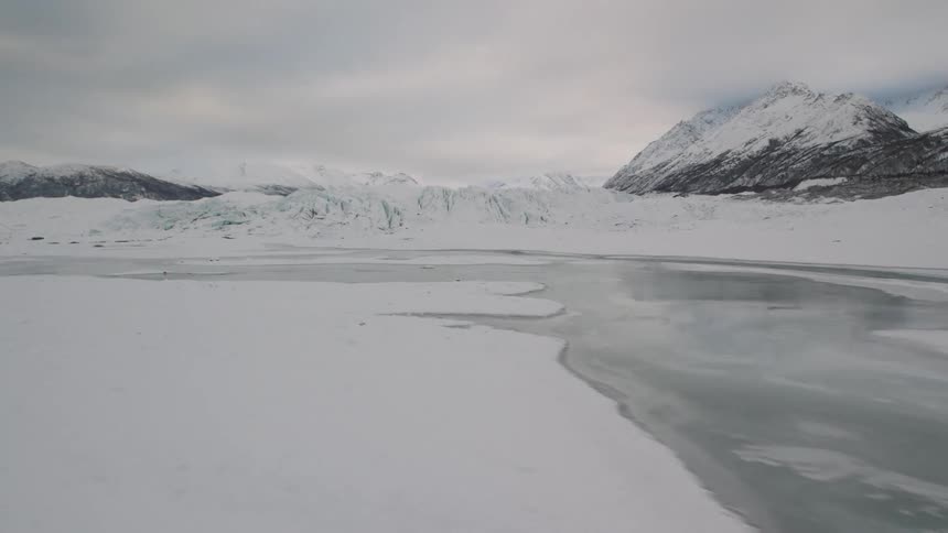 A frozen stream runs through an ice and snow covered landscape