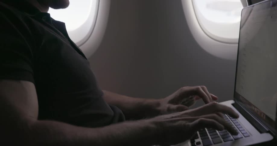 Man sitting in seat in airplane typing on laptop